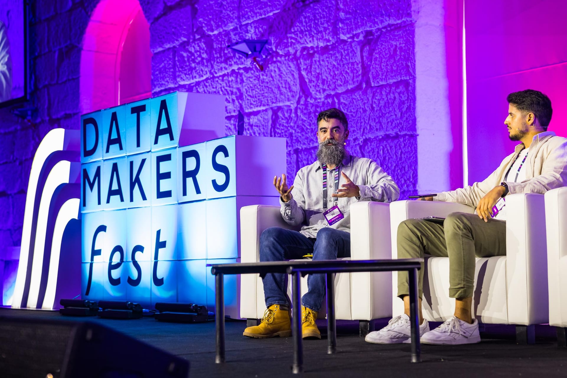 Ryan Chaves speaking on causal machine learning in a fireside chat at Data Makers Fest in Porto, seated beside the moderator in front of the illuminated event sign.